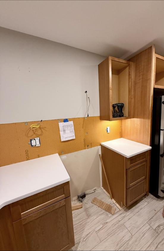 Kitchen cabinets and countertops mid-installation, floor plan taped to wall